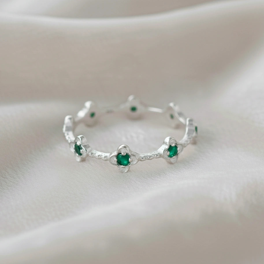 Sterling silver floral green onyx eternity band ring set with clover shaped stones angled straight on off-white velvet messy cloth.