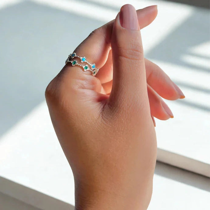 Two eternity band rings sterling silver floral design one green onyx one blue topaz on a woman's finger angled left close up.