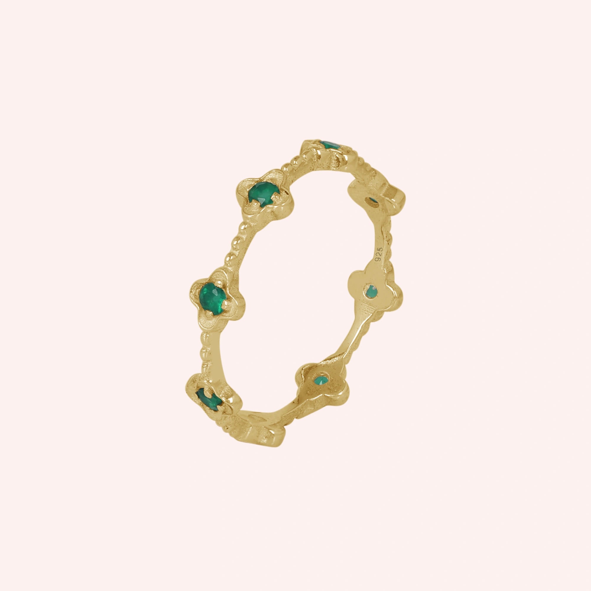 Gold plated floral green onyx eternity band ring set with clover shaped stones angled slightly left on a pink background.