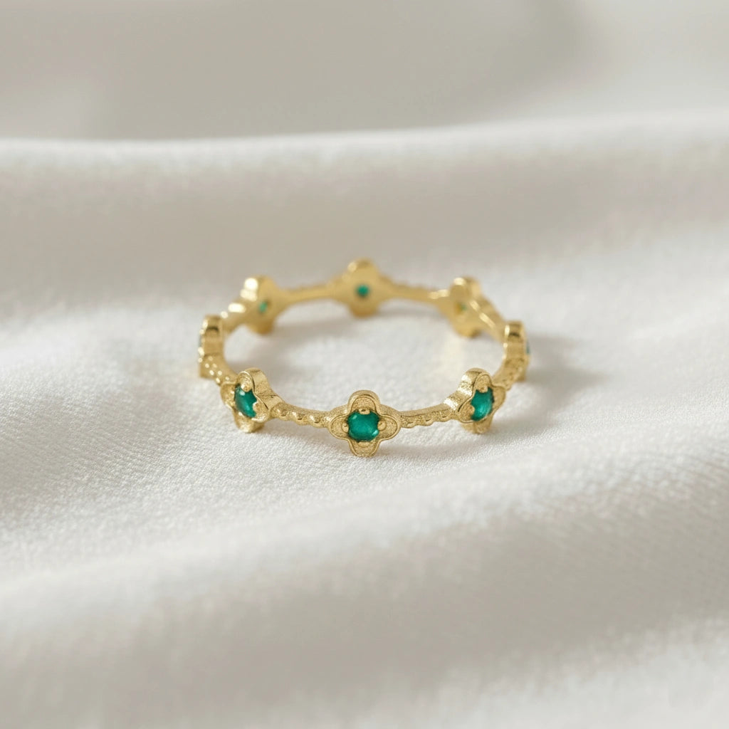 Gold plated green onyx floral eternity band ring set with clover shaped stones angled straight on off-white velvet messy cloth.