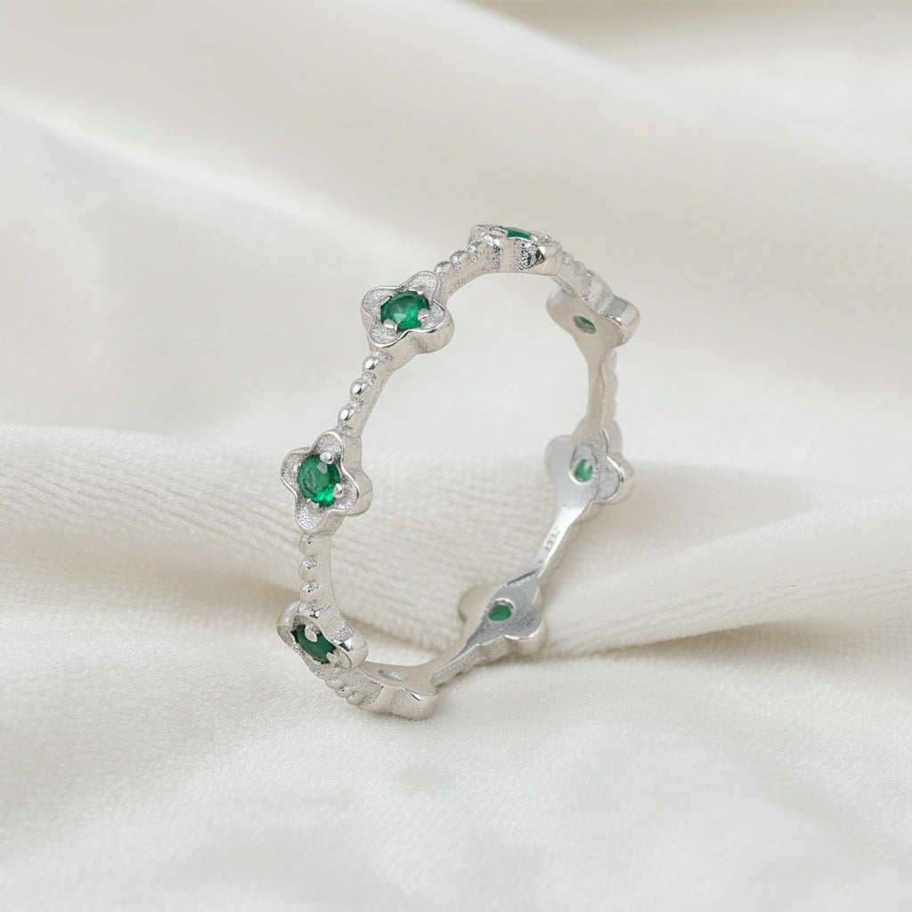 Sterling silver floral green onyx eternity band ring set with clover shaped stones angled slightly left on white velvet messy cloth.