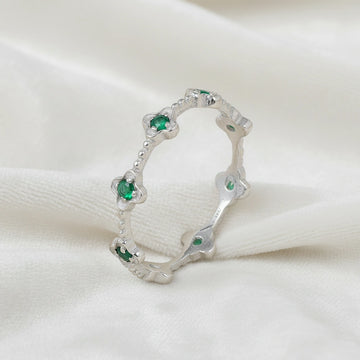 Sterling silver floral green onyx eternity band ring set with clover shaped stones angled slightly left on white velvet messy cloth.