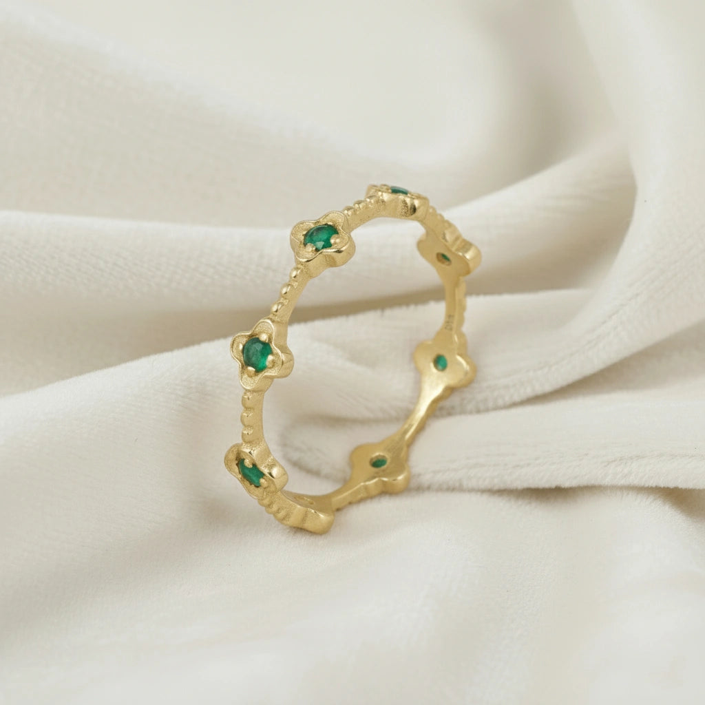 Gold plated green onyx floral eternity band ring set with clover shaped stones angled slightly left on white velvet messy cloth.