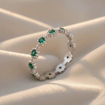 Diagonal close-up of a sterling silver onyx ring featuring detailed floral settings and dark green stones on flowing white velvet fabric