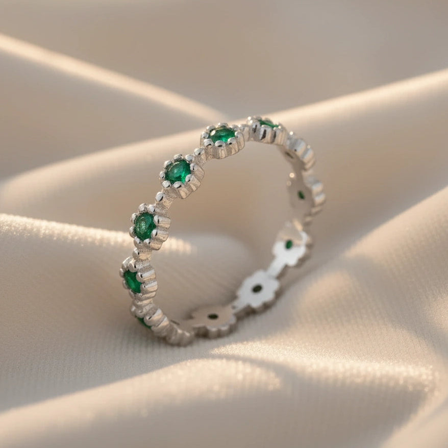 Diagonal close-up of a sterling silver onyx ring featuring detailed floral settings and dark green stones on flowing white velvet fabric