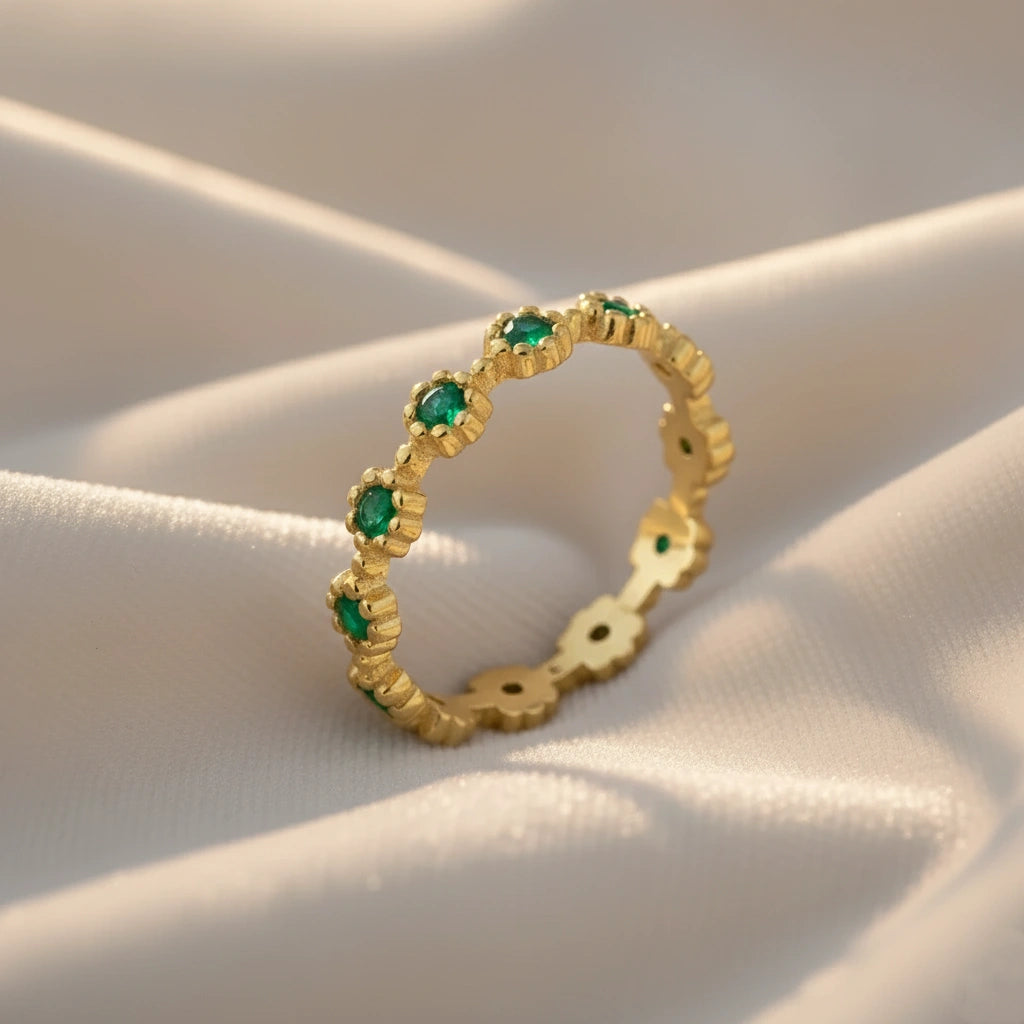 Angled gold vermeil onyx eternity ring on a draped white velvet background showcasing vibrant green onyx gemstones with detailed texture.