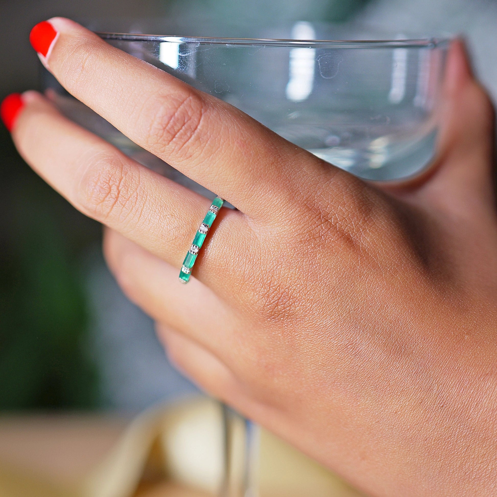 Gold-plated sterling silver green onyx ring with baguette stones on hand holding glass low angle with blurred background