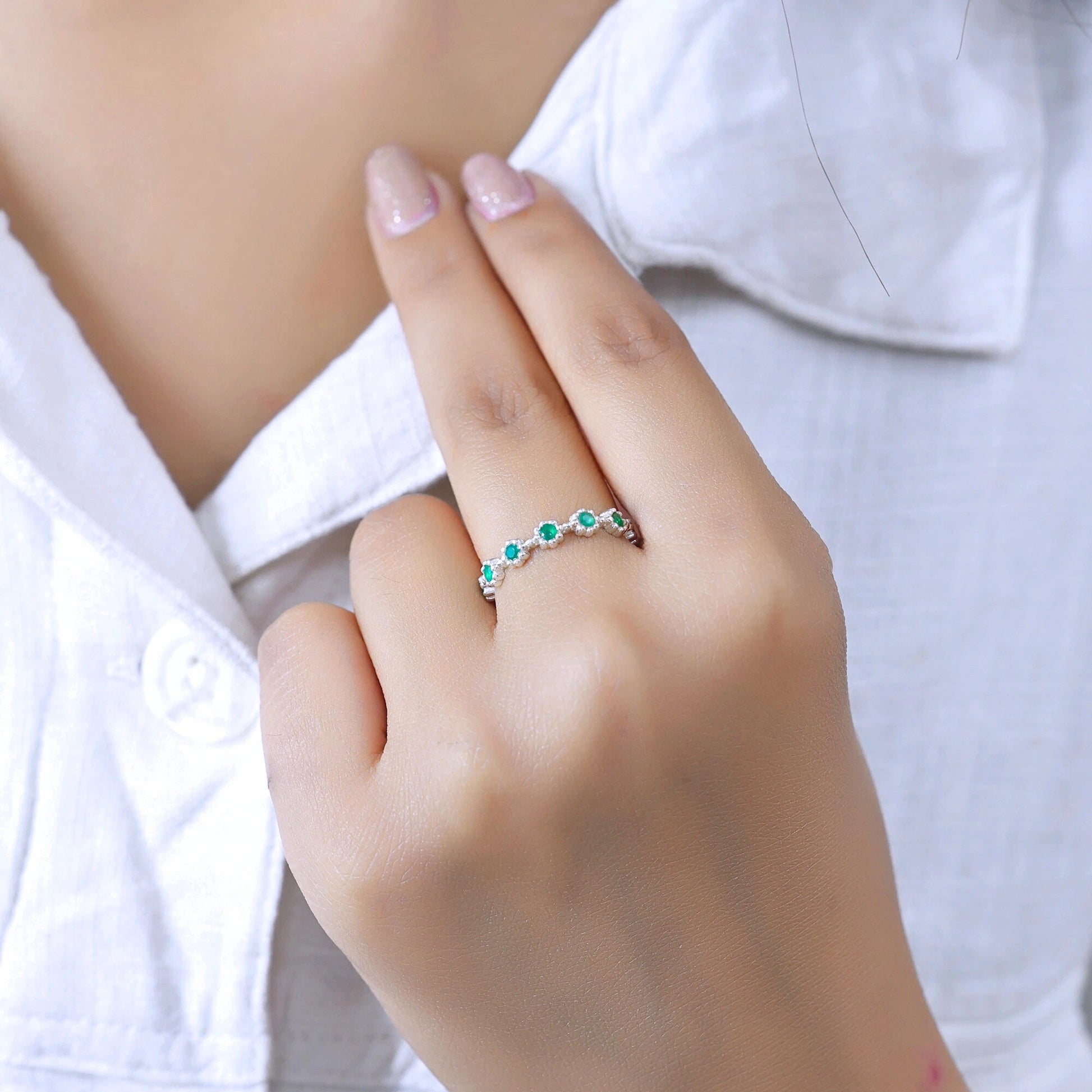 A sterling silver onyx eternity ring worn on a woman's finger over a shirt showcasing green onyx gemstones from a straight-on perspective.