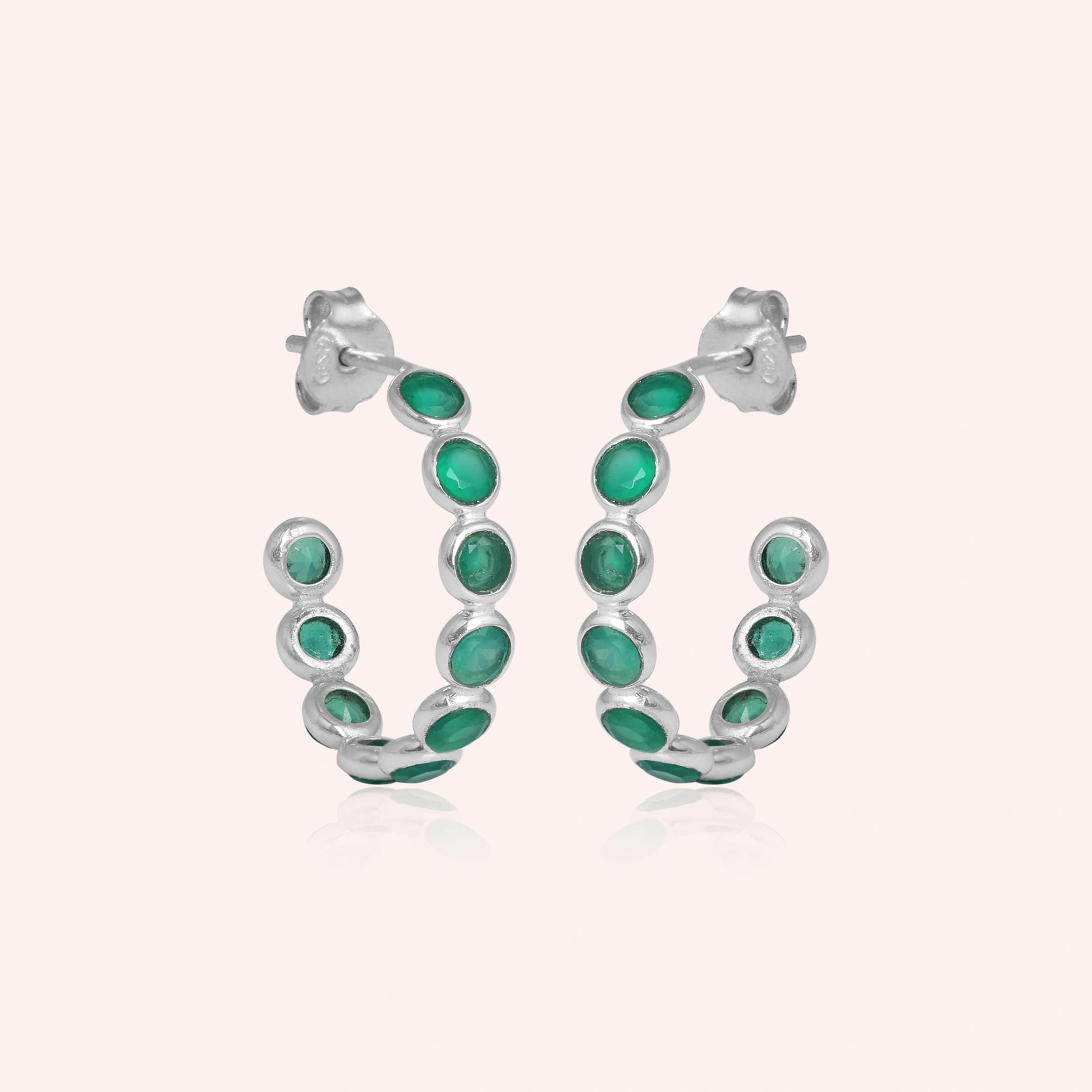 Sterling silver hoop earrings set with green onyx stones simple jewelry product shot on a light pink background straight on view.