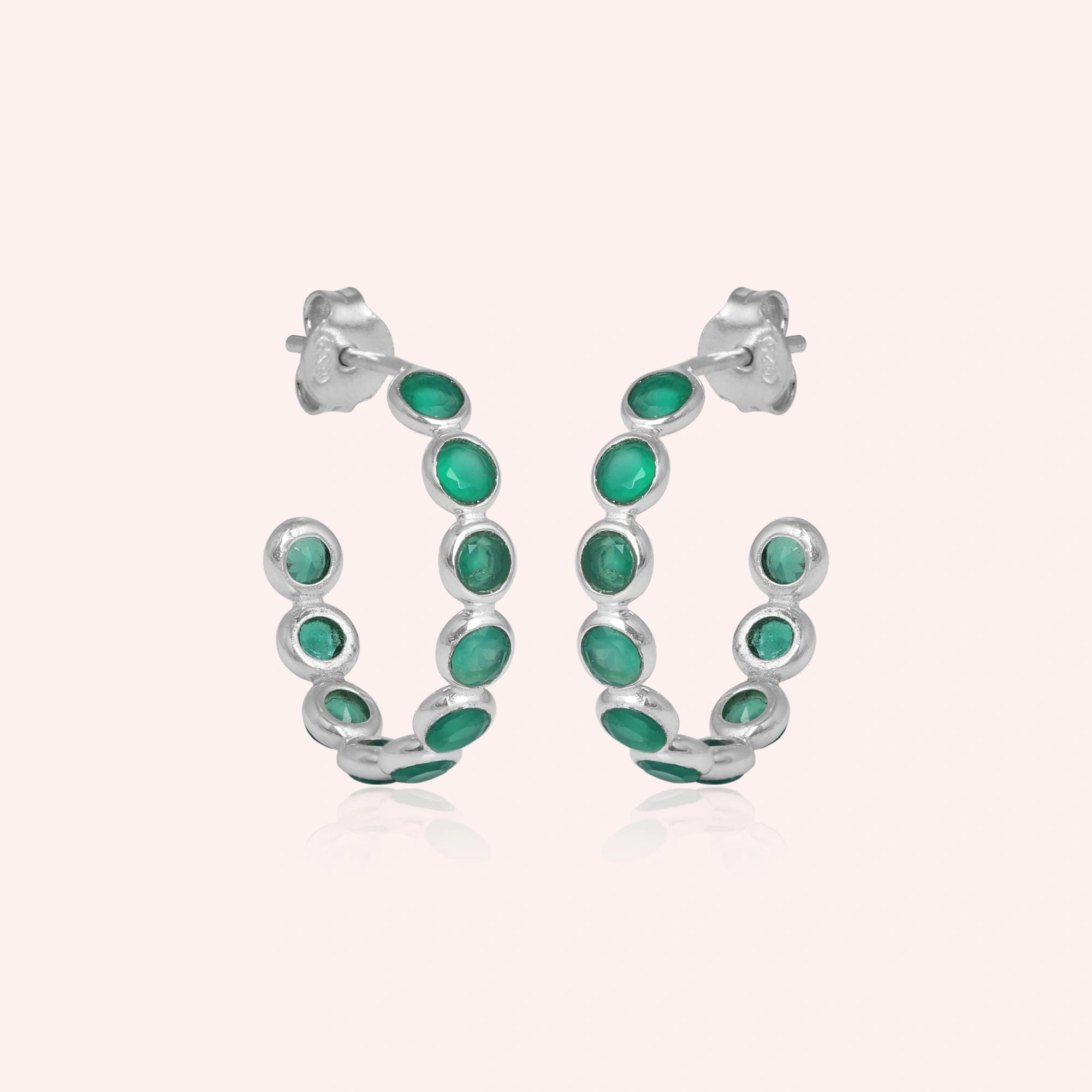 Sterling silver hoop earrings set with green onyx stones simple jewelry product shot on a light pink background straight on view.