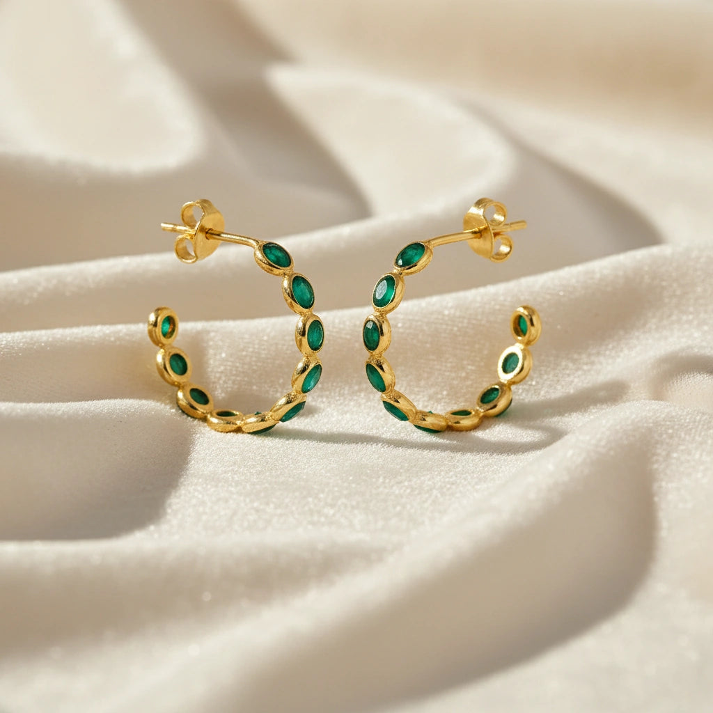 Gold vermeil onyx hoop earrings with bright green stones on a messy off white velvet fabric background angled for detail.