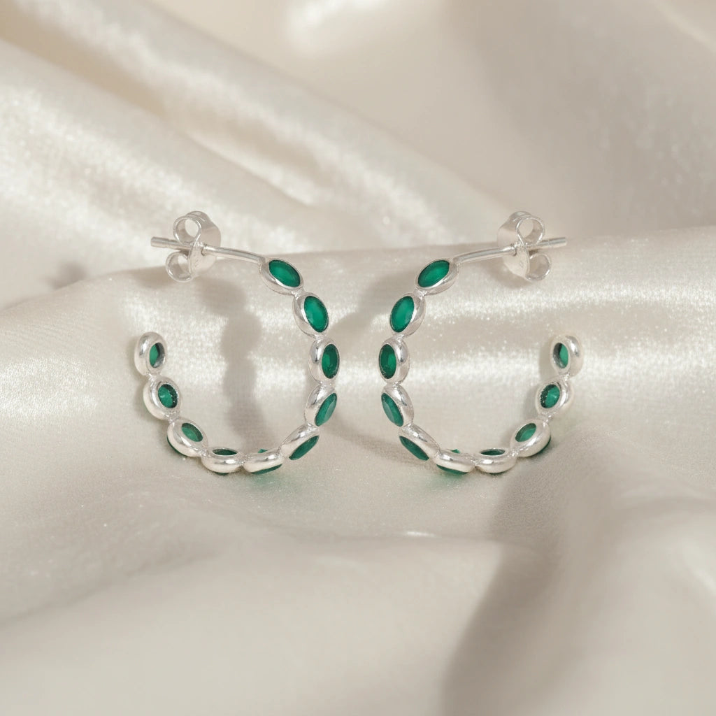 Sterling silver hoop earrings with bright green onyx stones on a wrinkled off white velvet fabric background angled for detail.