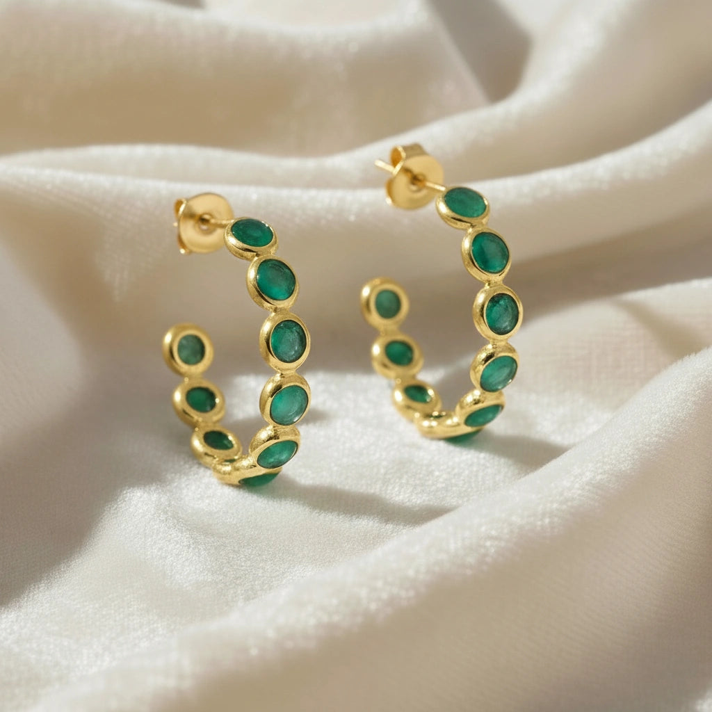 Gold vermeil onyx hoop earrings with bright green stones on a wrinkled off white velvet fabric background angled for detail.