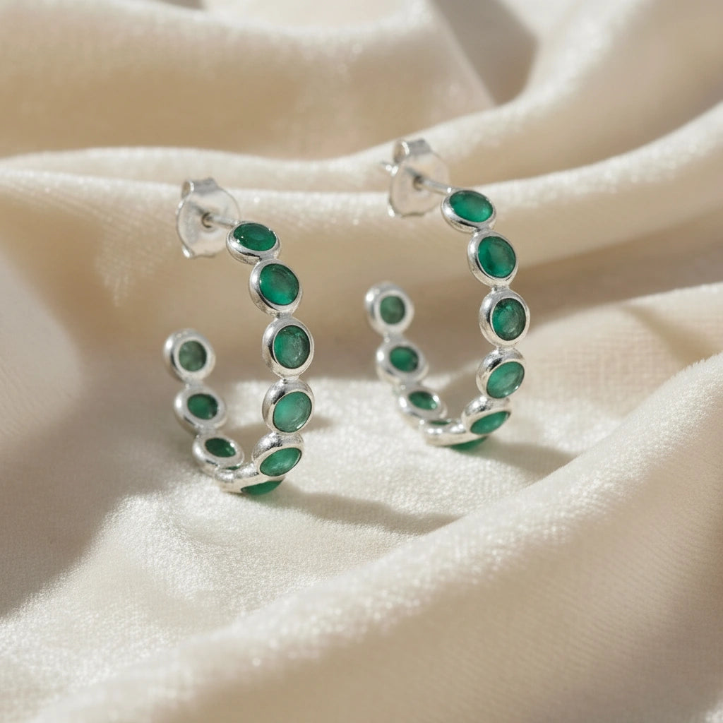 Sterling silver hoop earrings with bright green onyx stones on a wrinkled off white velvet fabric background angled for detail.