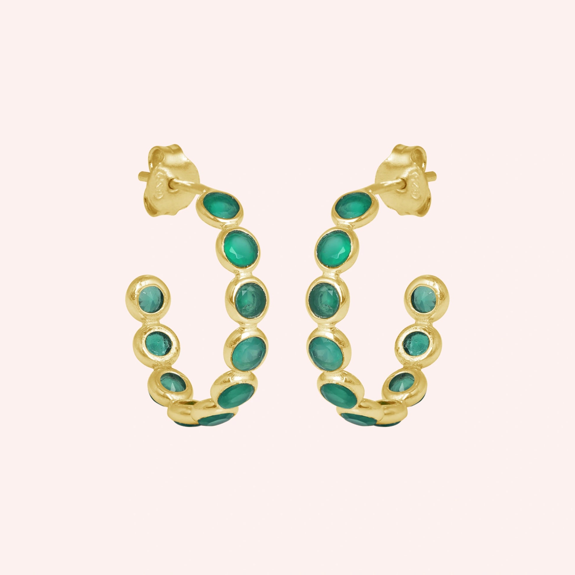 Gold vermeil onyx hoop earrings featuring green stones product focus on a minimal light pink background straight on view.