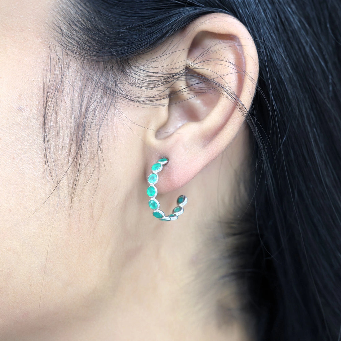 Sterling silver hoop earrings with bright green onyx stones on a wrinkled off white velvet fabric background angled for detail.