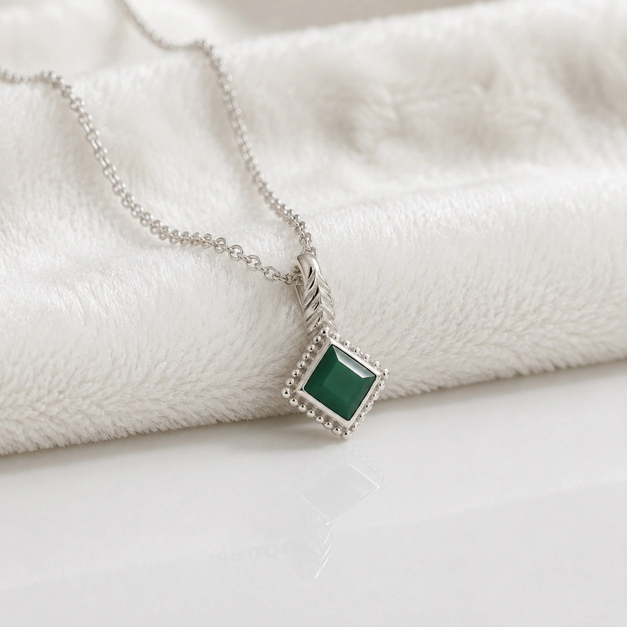 Birthstone_necklace_in_sterling_silver_with_square_cut_green_onyx_pendant_in_slighlty_angled_view_on_soft_white_fabric_background