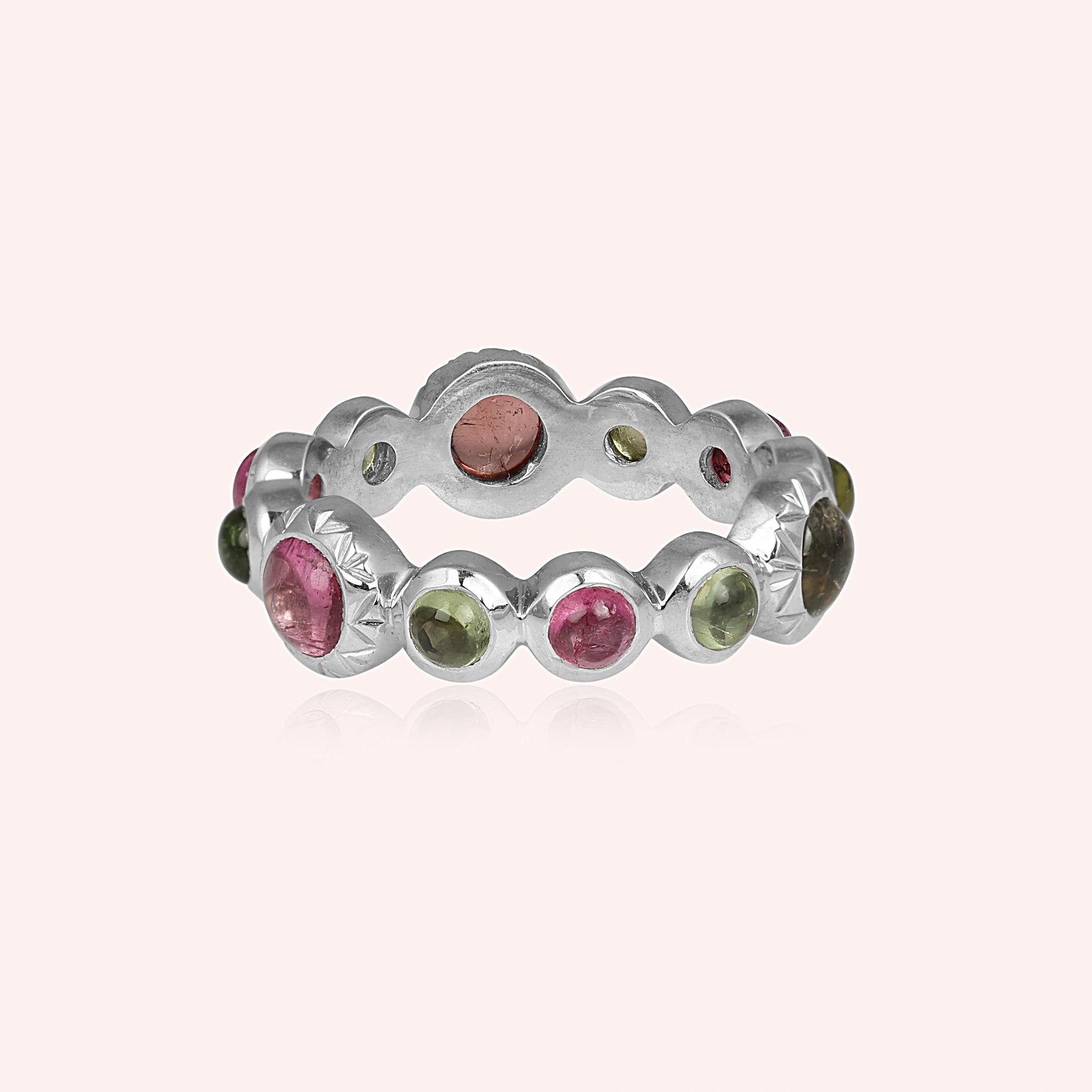 Striking silver eternity band ring with contrasting pink and green gemstones bezel set low angle on light pink background