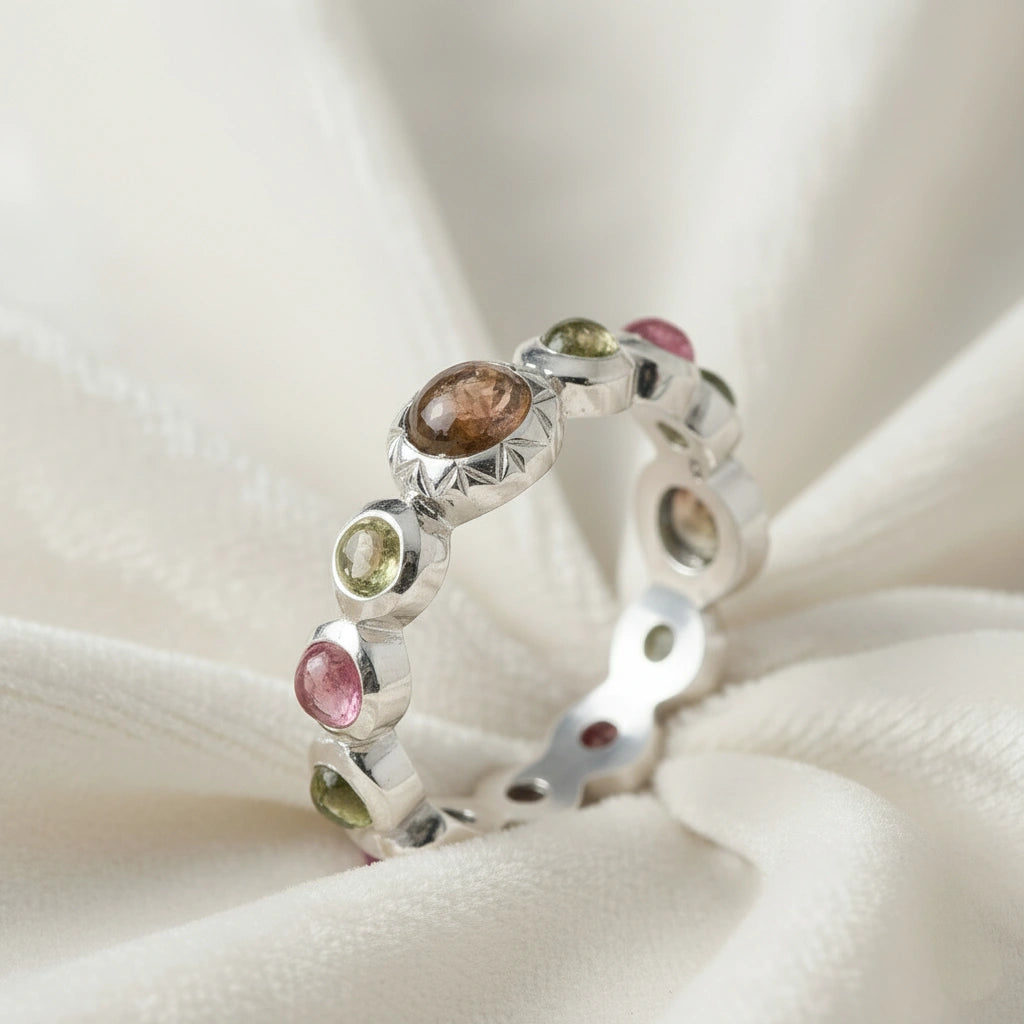 Silver eternity band ring with mixed color gemstones bezel set elevated angle view on soft white velvet fabric background