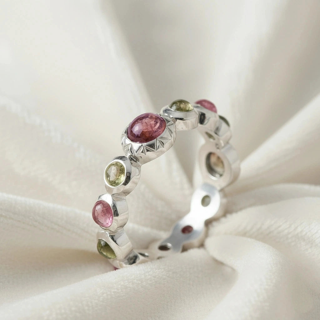 Silver eternity band ring with mixed color gemstones bezel set elevated angle view on soft white velvet fabric background