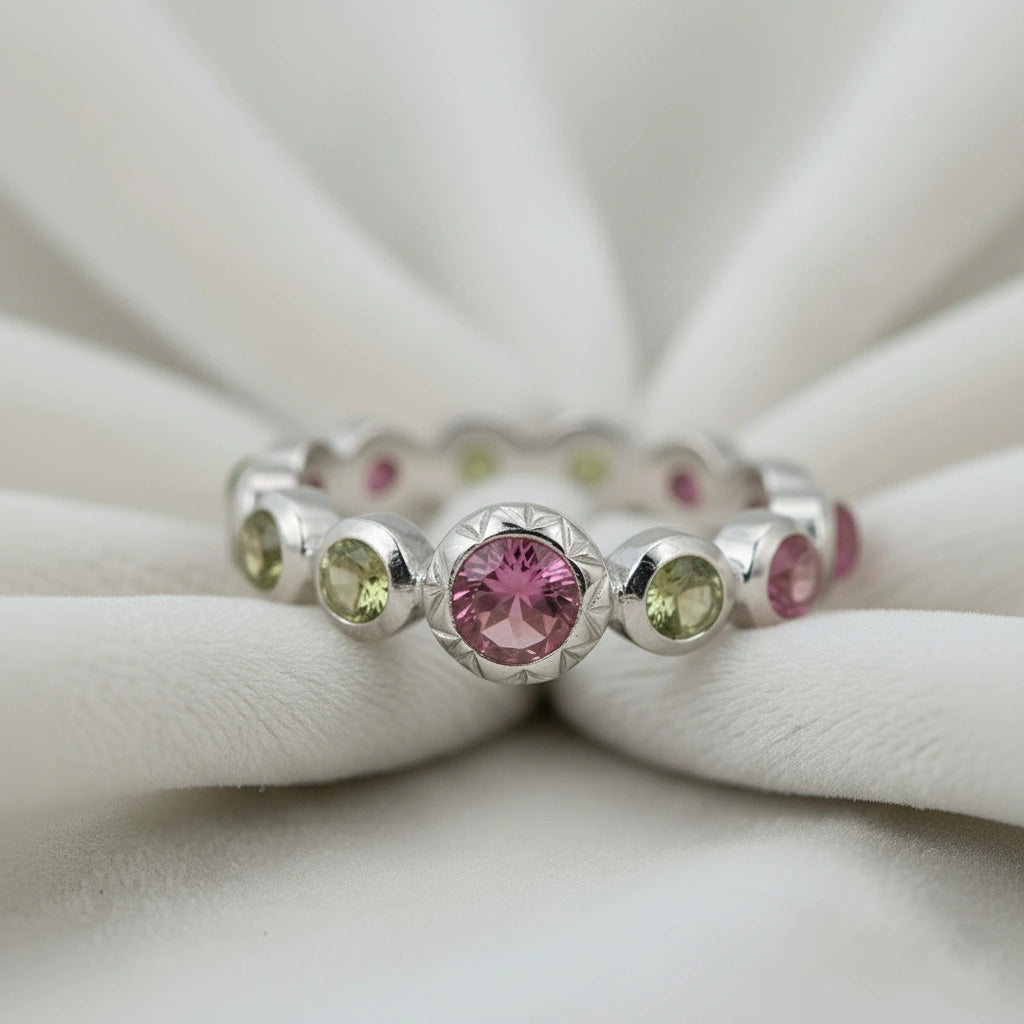 Silver eternity band ring with pink and green tourmaline gemstones bezel set low angle view on a white velvet fabric background