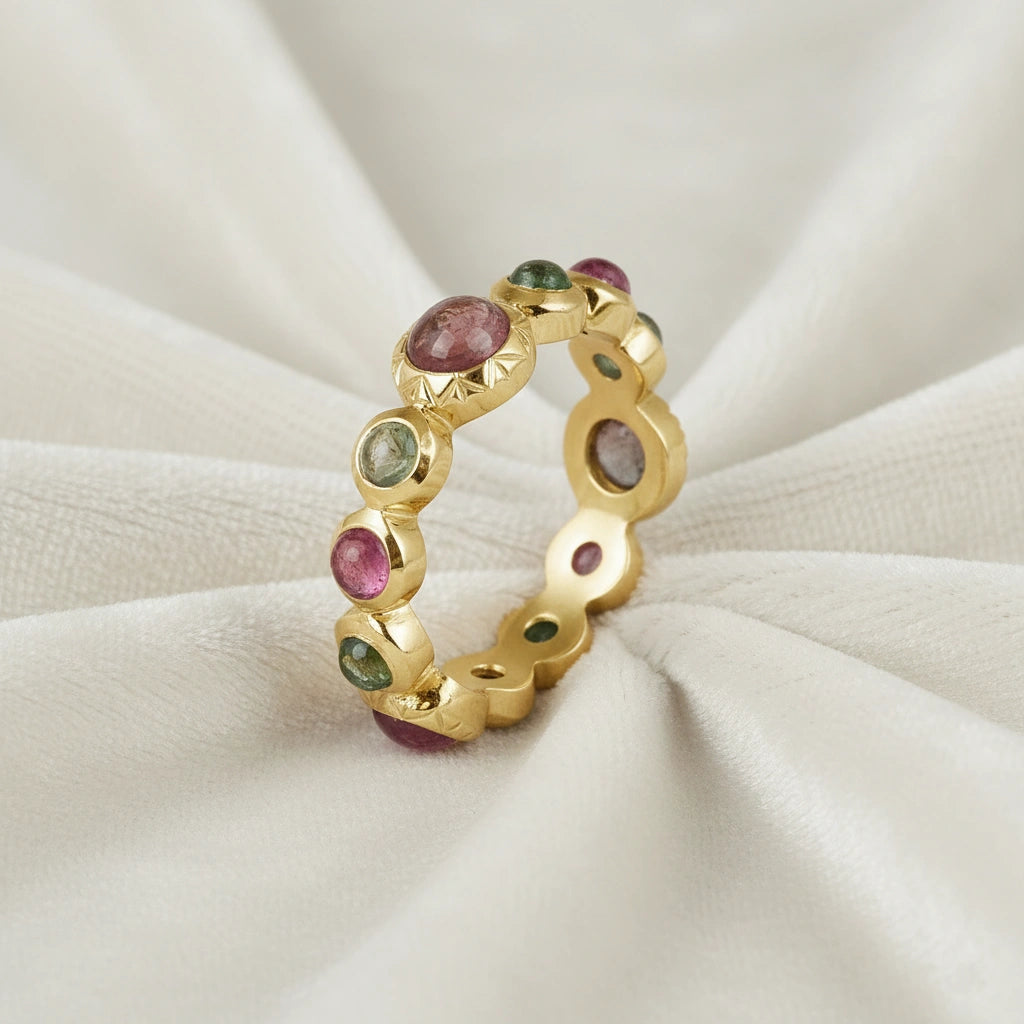 Gold-plated eternity band ring with mixed pink and green tourmaline gemstones elevated view on a white velvet fabric background