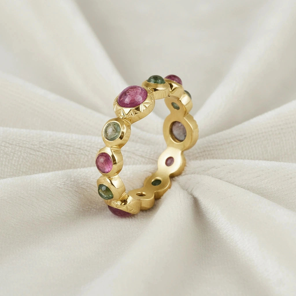 Gold-plated eternity band ring with mixed pink and green tourmaline gemstones elevated view on a white velvet fabric background