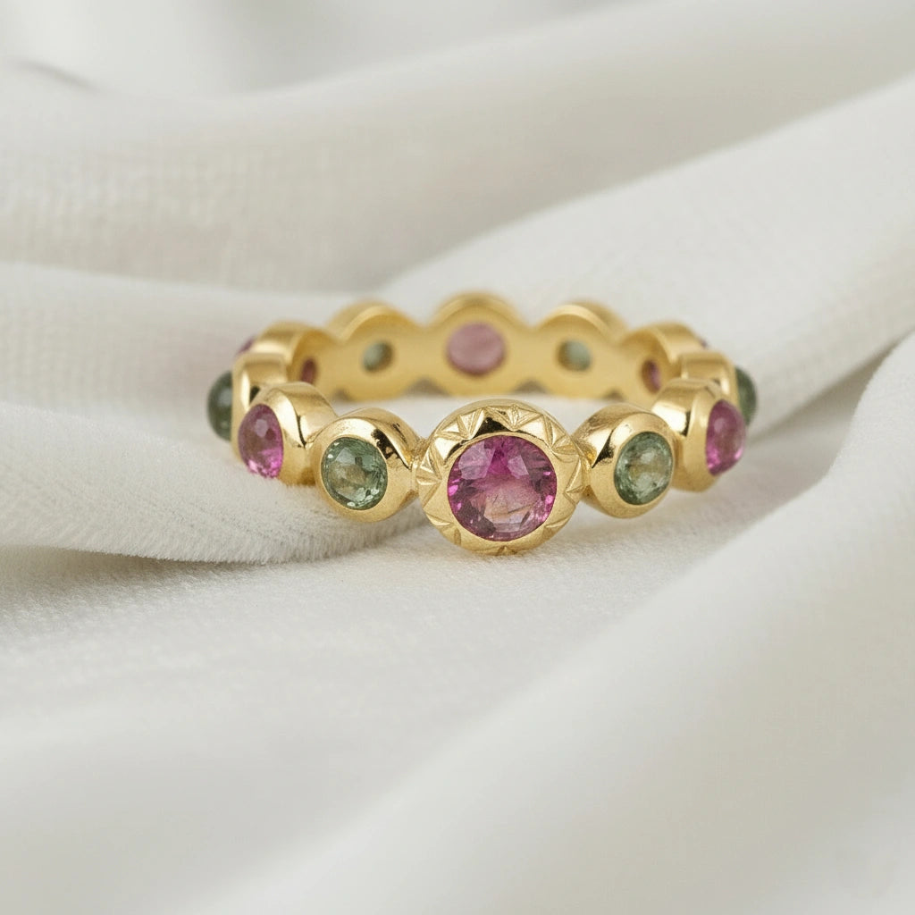 Gold-plated eternity band ring with pink and green tourmaline gemstones bezel set low angle view on white velvet fabric background