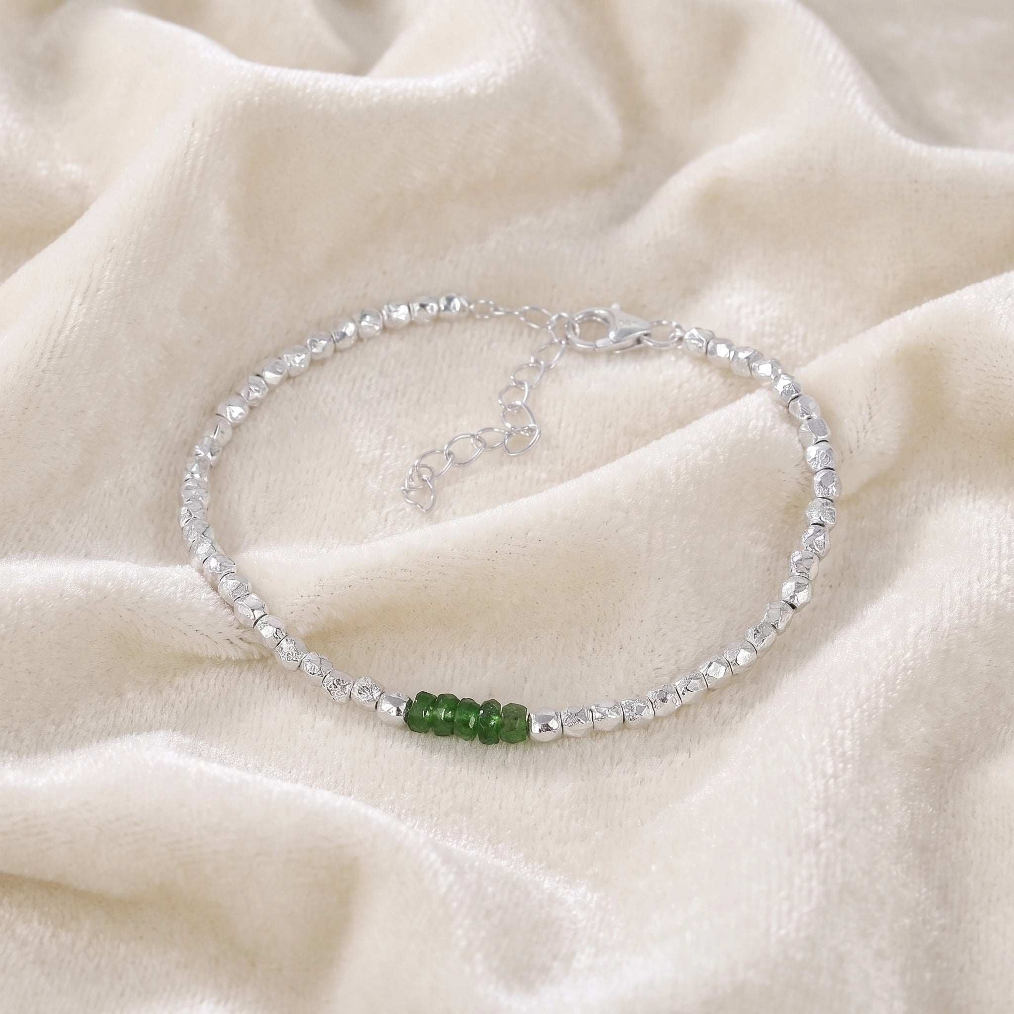 Green_stone_bracelet_with_green_onyx_stones_and_sterling_silver_beads_at_front_angle_view_on_soft_fabric_background