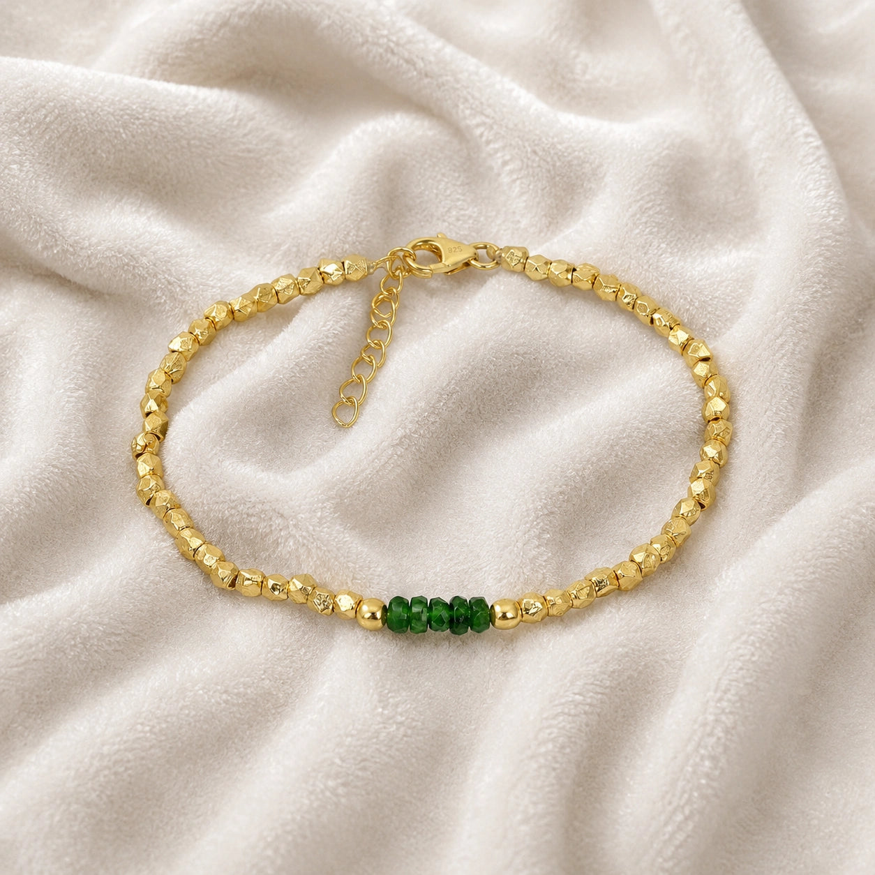 Green_stone_bracelet_with_green_onyx_stones_and_gold_plated_silver_beads_at_front_angle_view_on_soft_fabric_background
