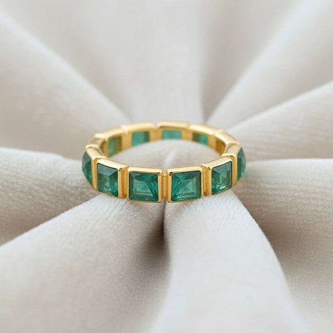 Center focus on a green onyx ring with square stones in a gold-plated eternity band sitting on soft creamy velvet folds.