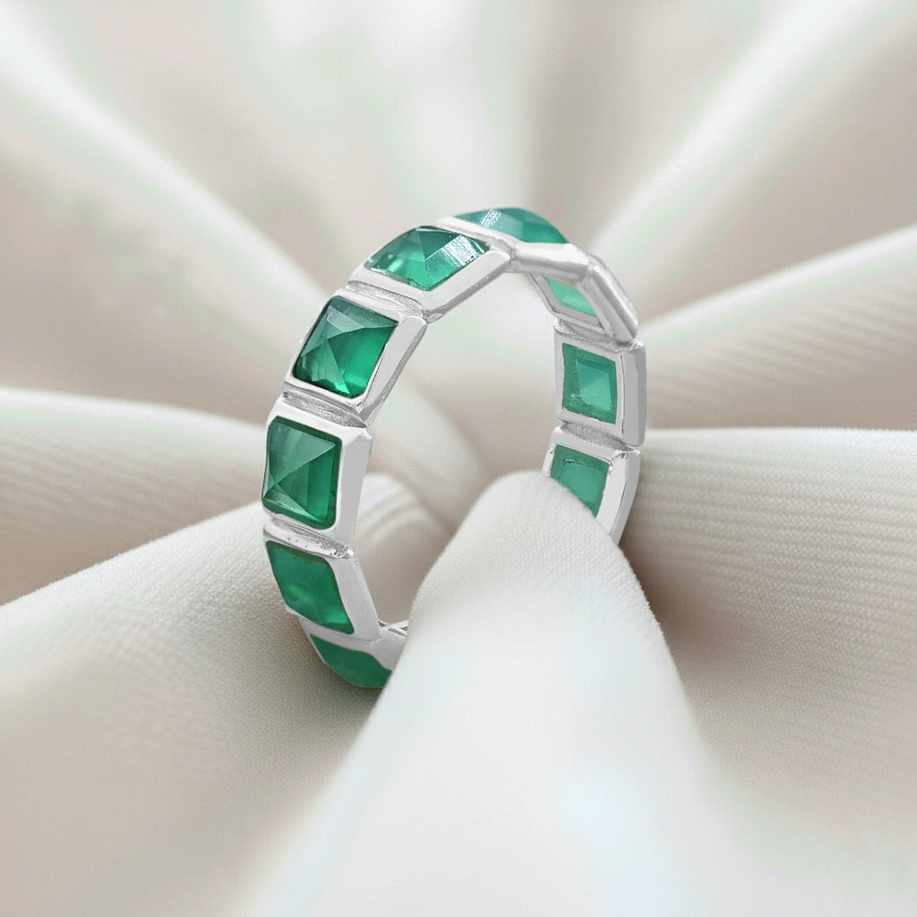 Up-close green onyx ring with square stones in a silver eternity band standing upright on a creamy white velvet drape.