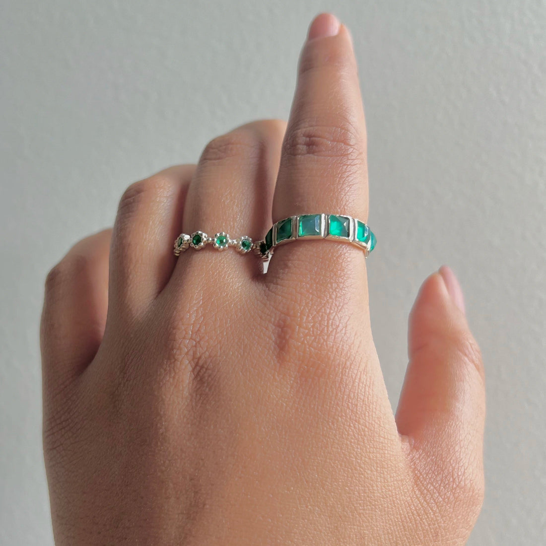 Up-close green onyx ring with square stones in a silver eternity band standing upright on a creamy white velvet drape.