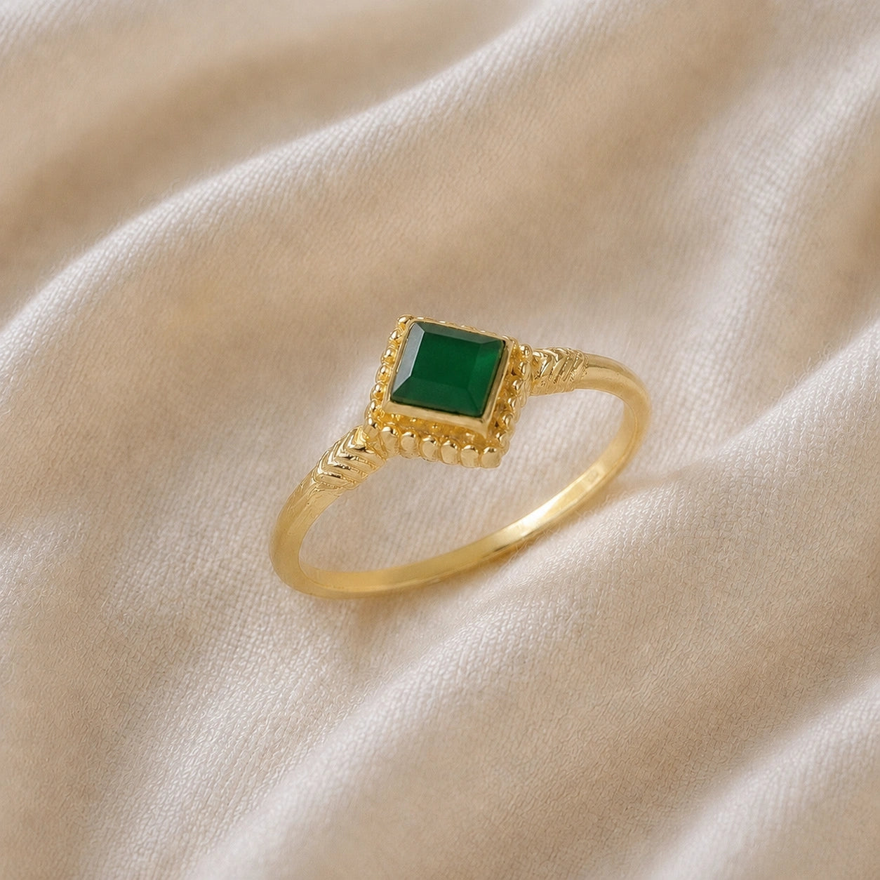 Princess_cut_ring_gold_plated_silver_with_square_green_onyx_and_detailed_band_slightly_tilted_view_on_soft_fabric_background