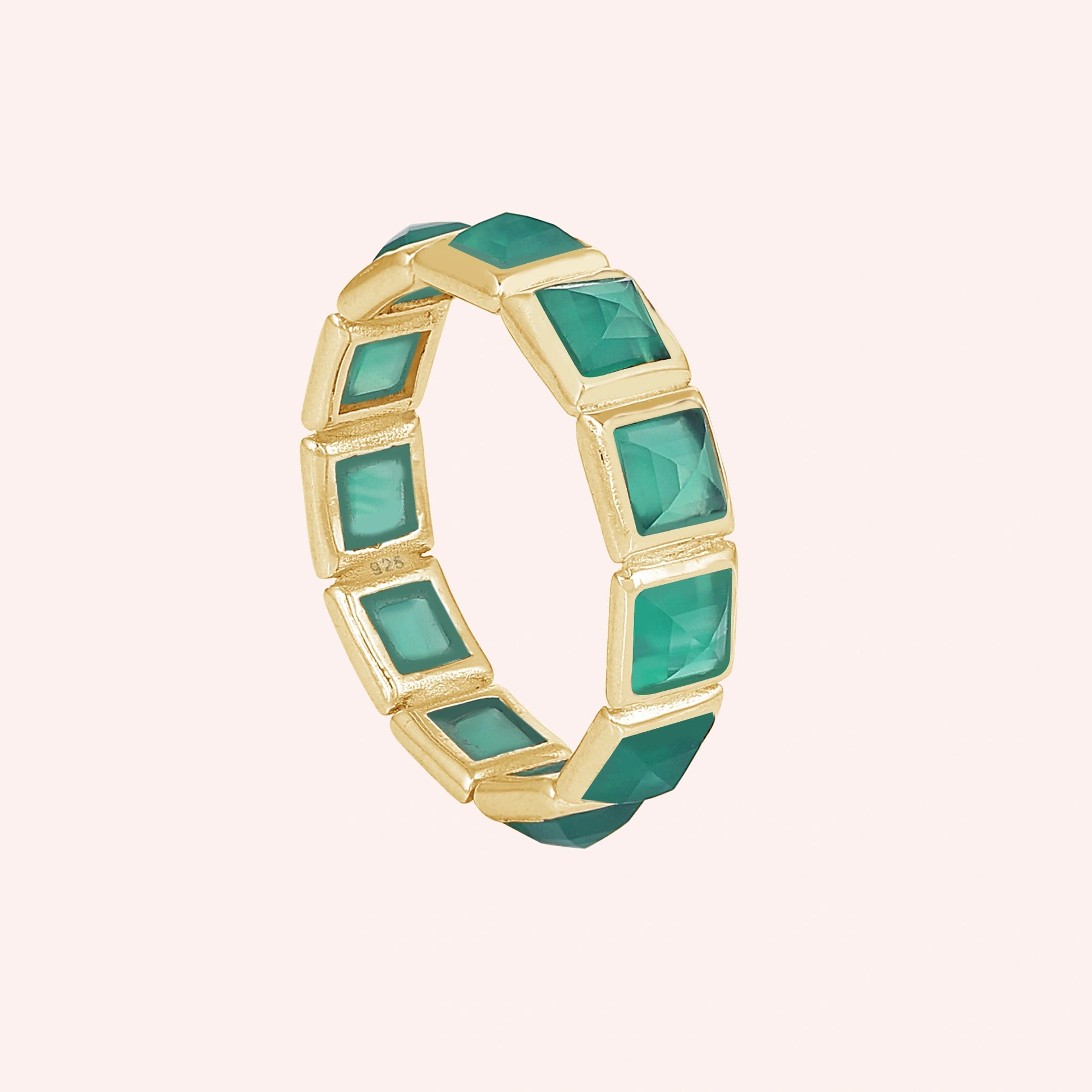 Angled shot of a gold-plated green onyx ring with square stones in a full eternity band set against a soft light pink backdrop