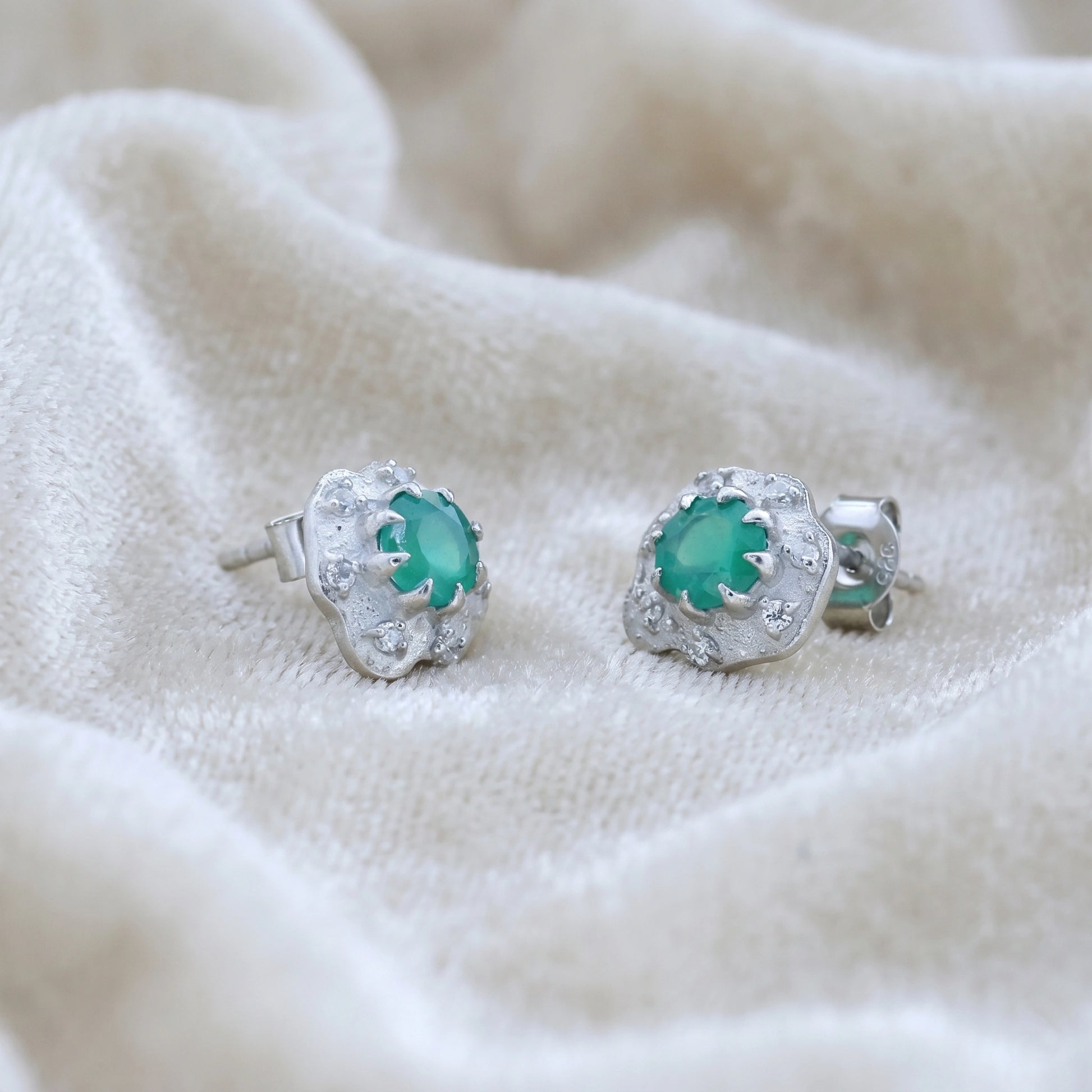 Halo_stud_earrings_in_sterling_silver_with_green_onyx_and_white_topaz_stones_at_slightly_angled_view_on_soft_fabric_background