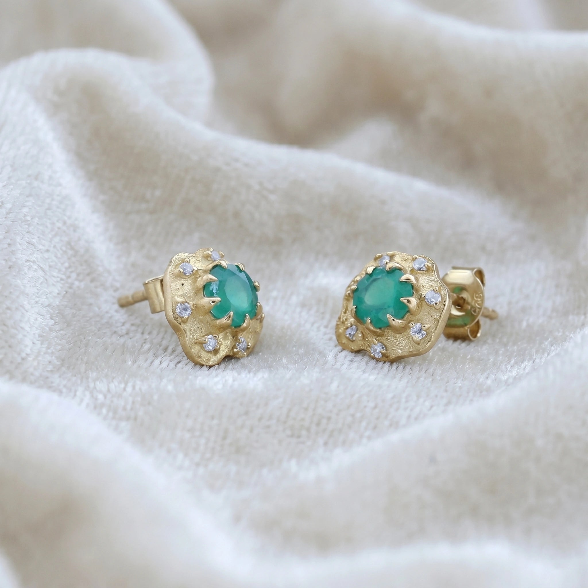 Halo_stud_earrings_in_gold_plated_silver_with_green_onyx_and_white_topaz_stones_at_slightly_angled_view_on_soft_fabric_background