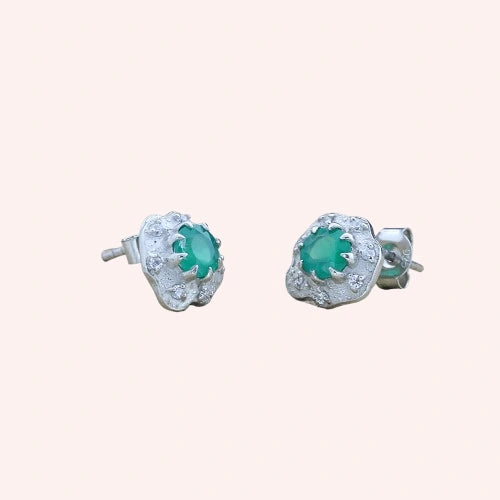 Halo_stud_earrings_in_sterling_silver_with_green_onyx_and_white_topaz_stones_at_slightly_angled_view_on_solid_pink_background