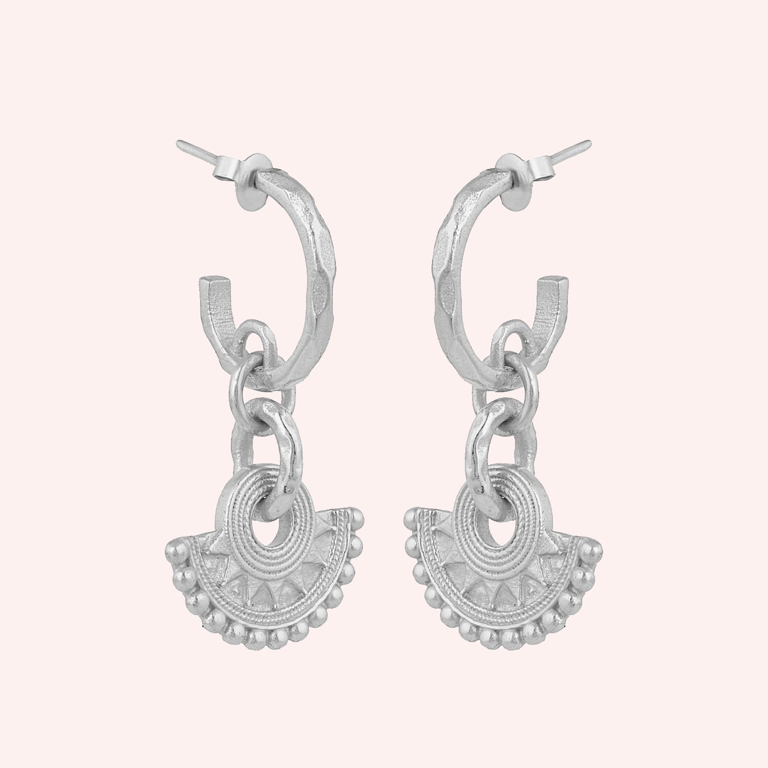 Handmade_earrings_in_sterling_silver_with_handcrafted_design_hoops_at_slight_angle_on_solid_pink_background