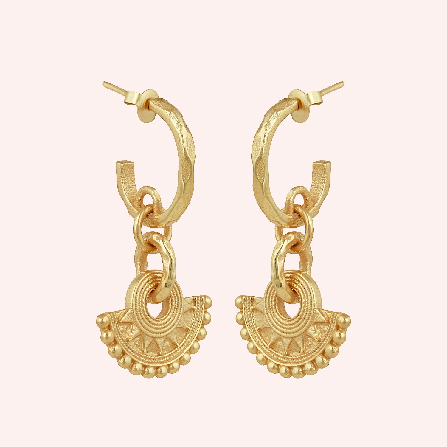 Handmade_earrings_in_gold_plated_silver_with_handcrafted_design_hoops_at_slight_angle_on_solid_pink_background