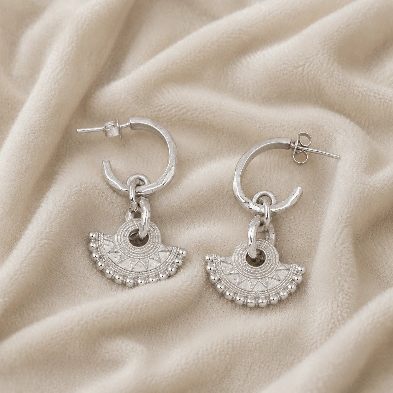 Handmade_earrings_in_sterling_silver_with_handcrafted_design_hoops_at_slight_angle_on_soft_fabric_background