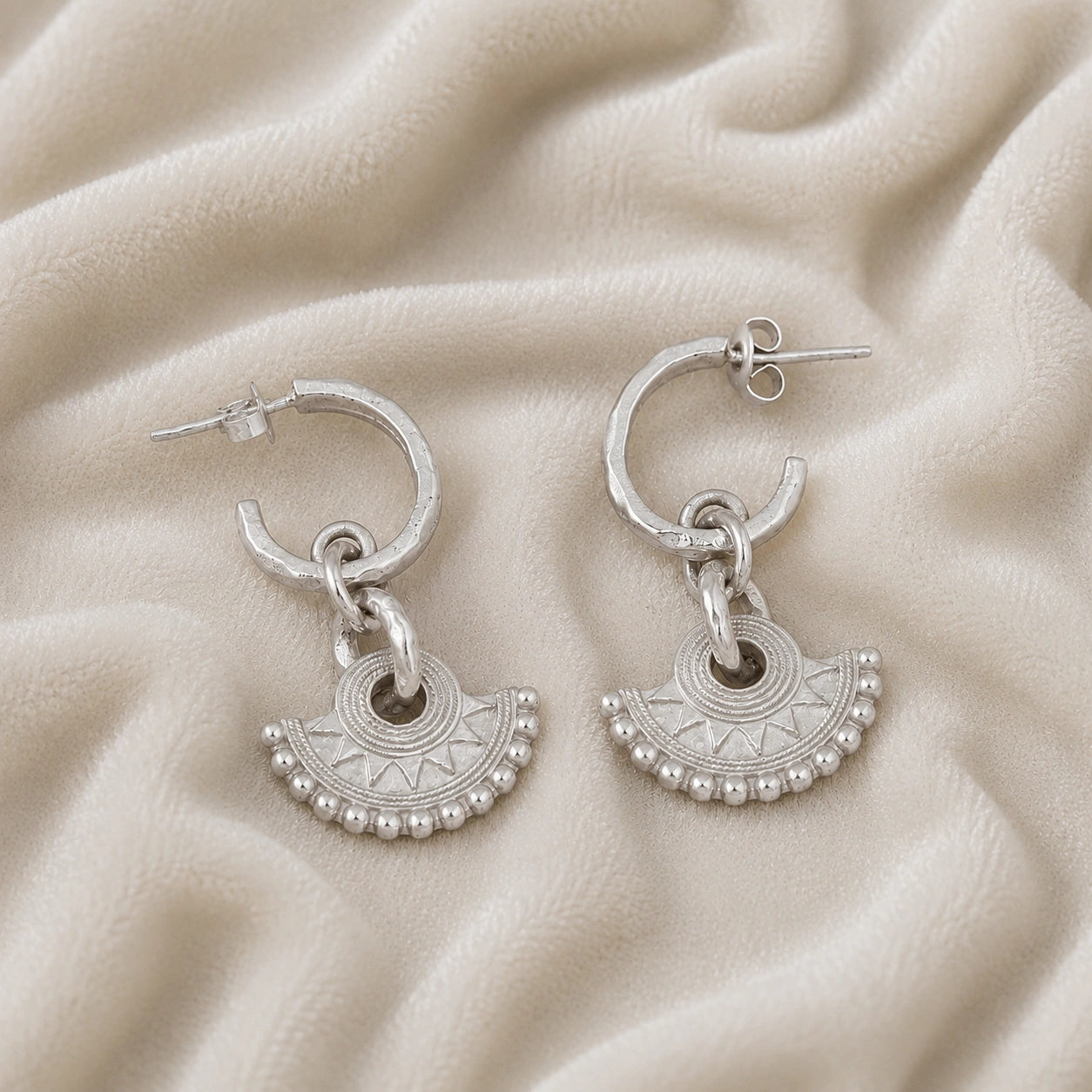 Handmade_earrings_in_sterling_silver_with_handcrafted_design_hoops_at_front_angle_on_soft_fabric_background