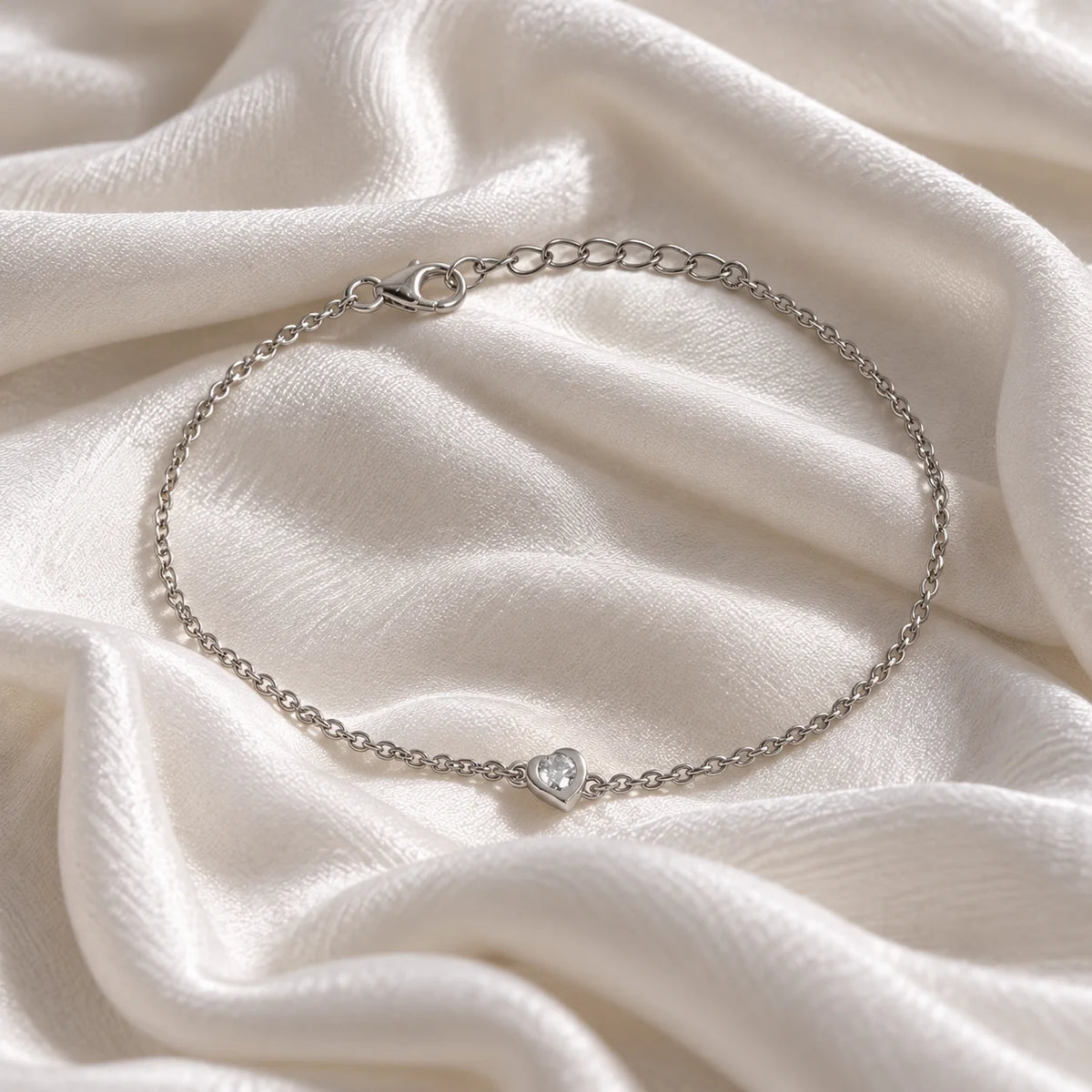 Heart_bracelet_in_sterling_silver_with_a_small_CZ_stone_at_front_angle_view_on_soft_fabric_background
