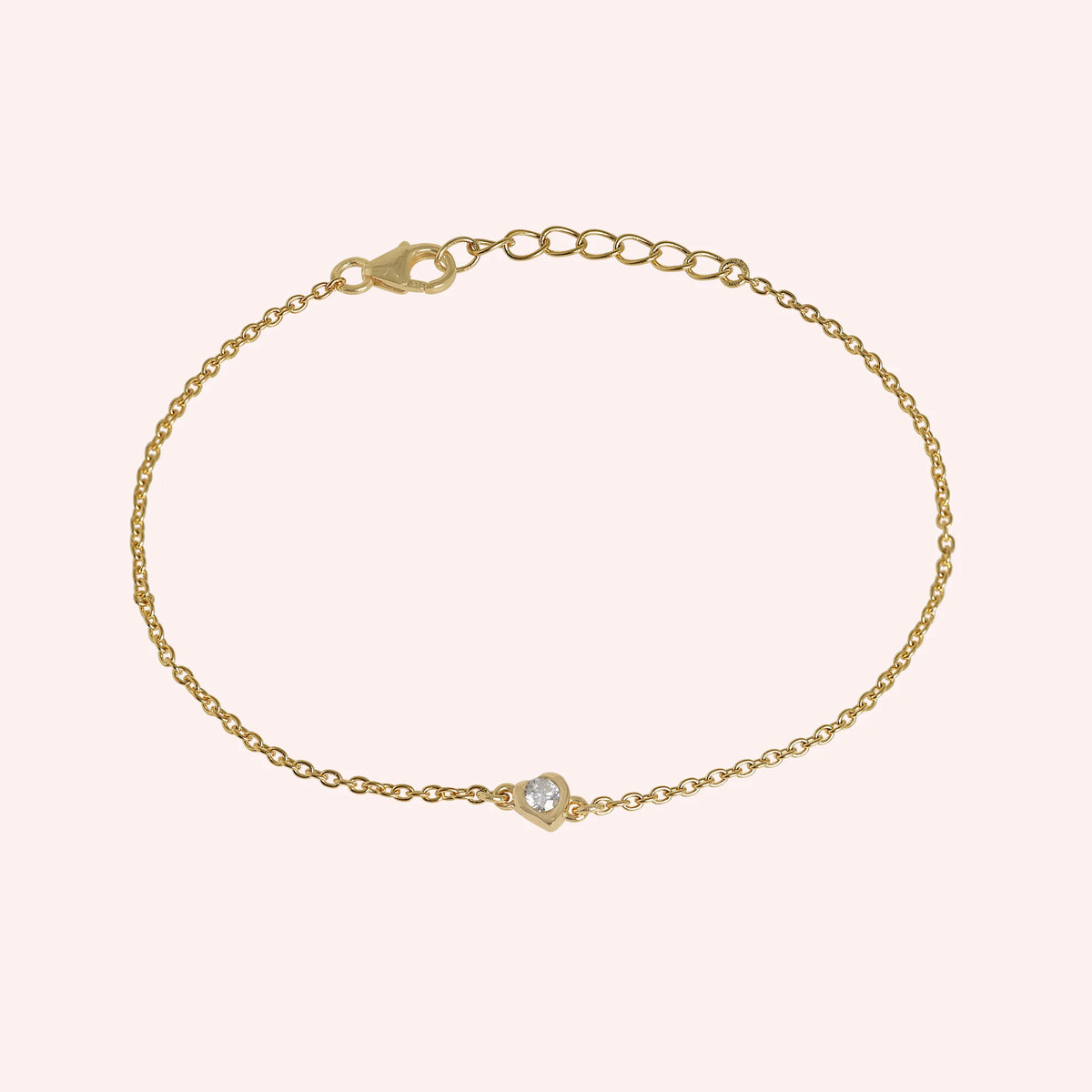 Heart_bracelet_in_gold_plated_silver_with_a_small_CZ_stone_at_front_angle_view_on_solid_pink_background