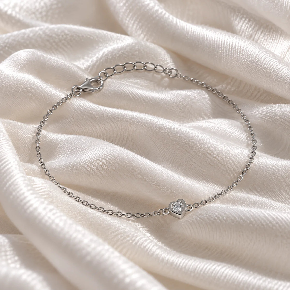 Heart_bracelet_in_sterling_silver_with_a_small_lab_grown_diamond_at_slight_angle_view_on_soft_fabric_background