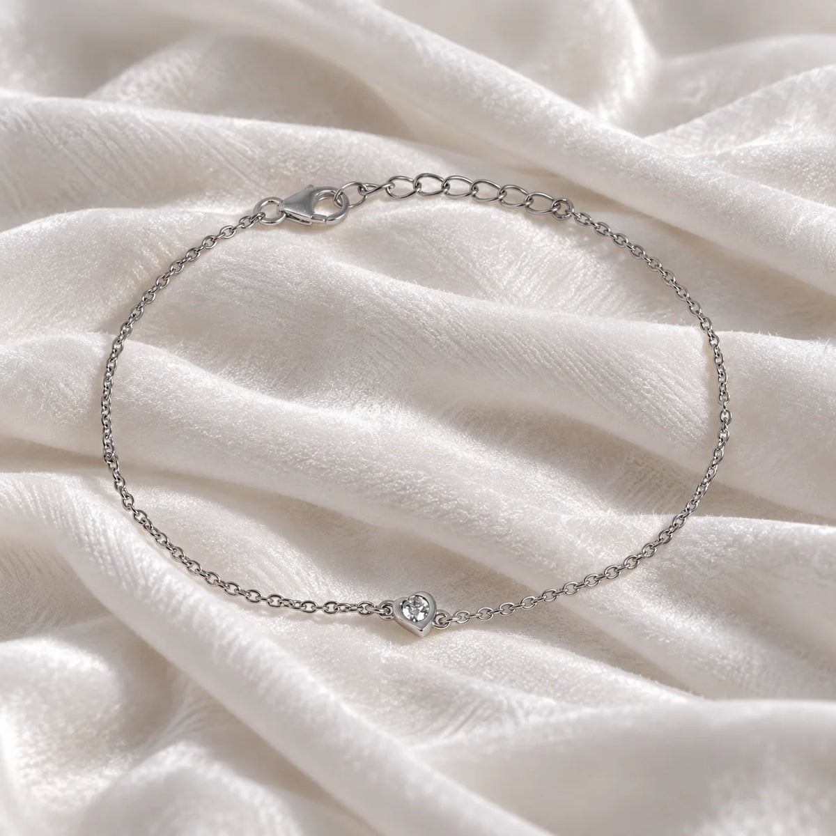 Heart_bracelet_in_sterling_silver_with_a_small_lab_grown_diamond_at_front_angle_view_on_soft_fabric_background