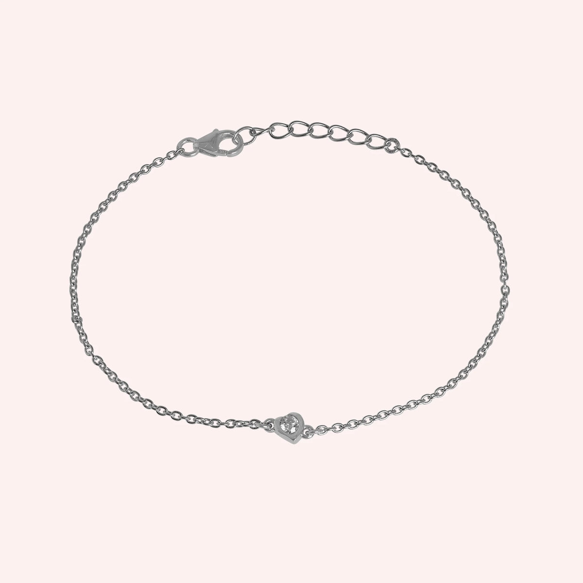 Heart_bracelet_in_sterling_silver_with_a_small_lab_grown_diamond_at_slight_angle_view_on_solid_pink_background