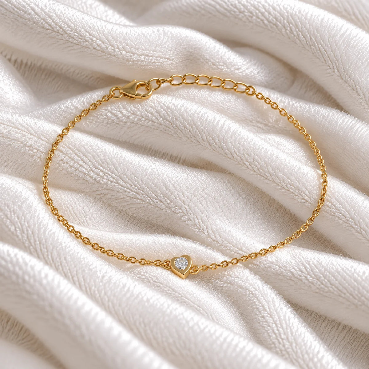 Heart_bracelet_in_gold_plated_silver_with_a_small_CZ_stone_at_front_angle_view_on_soft_fabric_background