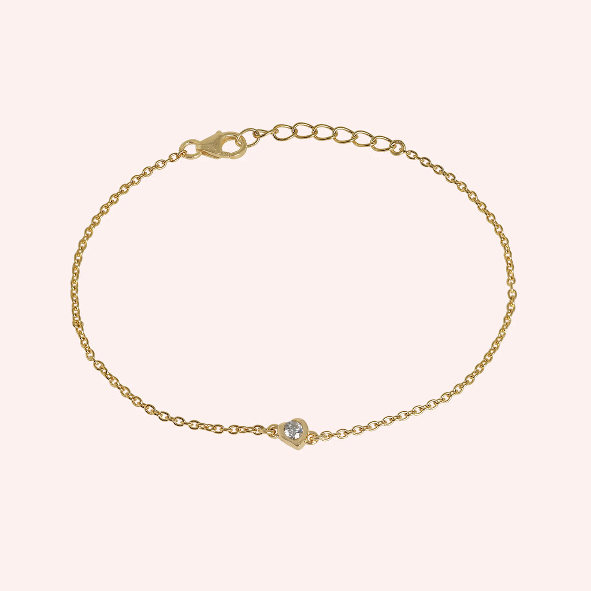 Heart_bracelet_in_gold_plated_silver_with_a_small_lab_grown_diamond_at_slight_angle_view_on_solid_pink_background