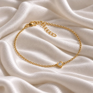 Heart_bracelet_in_gold_plated_silver_with_a_small_CZ_stone_at_side_angle_view_on_soft_fabric_background